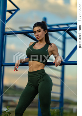 Girl in athletic wear confidently poses on sports ground with vibrant sky and sea in background Capturing essence of fitness and beauty at dusk 127299028