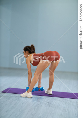 Athlete engages in a wide stance Romanian deadlift with dumbbells demonstrating strength and focus in a well equipped gym. The setting includes exercise mats and fitness equipment. Athlete engages in a wide stance Romanian deadlift with dumbbells demonstrating strength and focus in a well equipped gym. The setting includes exercise mats and fitness equipment. 127299099