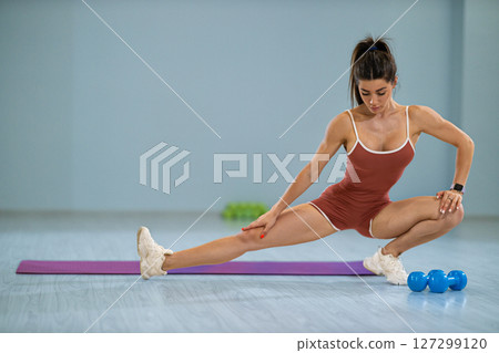 sporty girl performs left lunge stretch purple mat enhance flexibility in bright indoor fitness space with weights nearby Her focused posture showcases strength and dedication 127299120