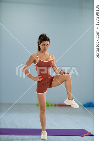 girl athlete is engaged in a standing side knee raise demonstrating her fitness skills in a well lit exercise studio. The setup includes workout equipment and a purple mat. 127299138