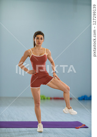 Girl athlete executes a standing side knee raise in a bright fitness studio. She focuses on maintaining balance and strength showcasing her athletic skills and dedication to fitness. Girl athlete executes a standing side knee raise in a bright fitness studio. She focuses on maintaining balance and strength showcasing her athletic skills and dedication to fitness. 127299139