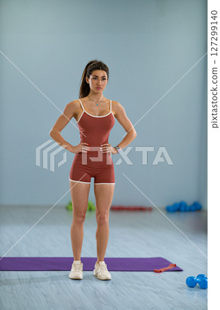 girl athlete focuses on her balance while executing a standing side knee raise in a fitness studio. The workout aims to enhance strength and stability surrounded by exercise equipment. girl athlete focuses on her balance while executing a standing side knee raise in a fitness studio. The workout aims to enhance strength and stability surrounded by exercise equipment. 127299140
