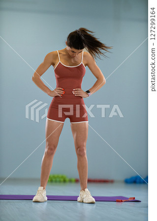 girl athlete performs head rotations in a circular motion to improve her coordination and balance. She is focusing intently in a training studio filled with exercise equipment. 127299164