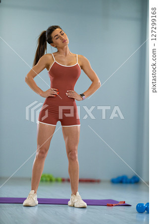 girl athlete stands in a gym tilting her head to the right and left. She wears a fitted outfit and appears focused while engaging in a warm up routine. 127299168