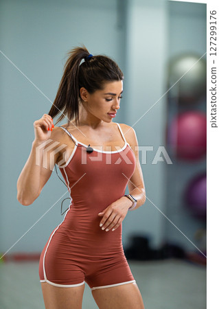 sporty girl announcer interacts with her audience while showcasing fitness activities in a well lit gym She is dressed in a fitted outfit, demonstrating confidence and energy 127299176
