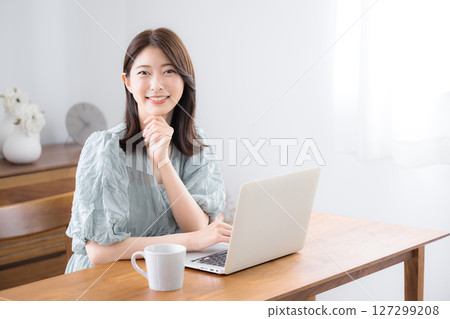 Young pretty woman in casual clothes using laptop in her home room, looking at camera Young pretty woman in casual clothes using laptop in her home room, looking at camera 127299208