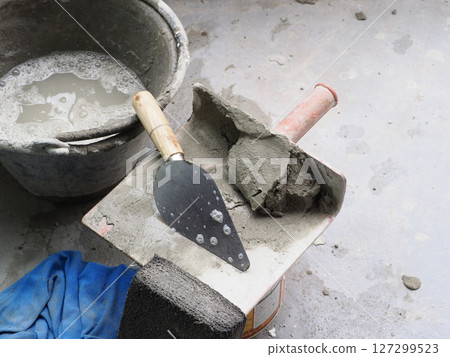 A cement and tool on floor seems worn but gray color palette creates sense of grit and determination in craftsmanship A cement and tool on floor seems worn but gray color palette creates sense of grit and determination in craftsmanship 127299523