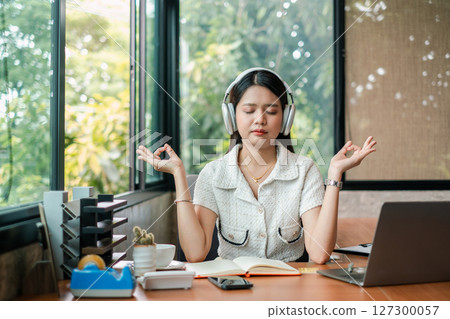 Woman practicing meditation with headphones in a modern office, promoting relaxation and focus. 127300057