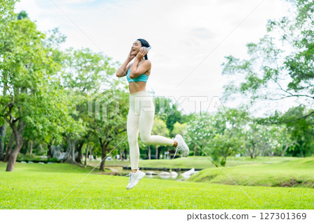 Young Asian woman in sportswear jumping happily during outdoor workout in a green park Young Asian woman in sportswear jumping happily during outdoor workout in a green park 127301369