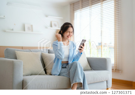 Smiling pretty young Asian woman sitting on cozy couch 127301371