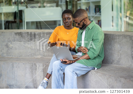 Focused African American multiracial couple work on laptop outdoors, prepare for exams, remote study 127301439