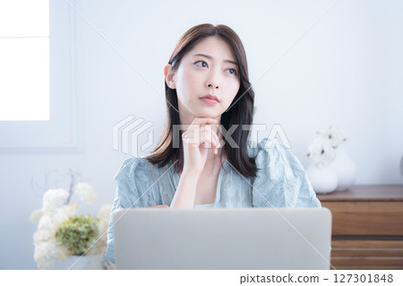 A cute woman thinking and wondering at her computer in her room. A slightly serious negative image. What should I do about changing jobs? A cute woman thinking and wondering at her computer in her room. A slightly serious negative image. What should I do about changing jobs? 127301848
