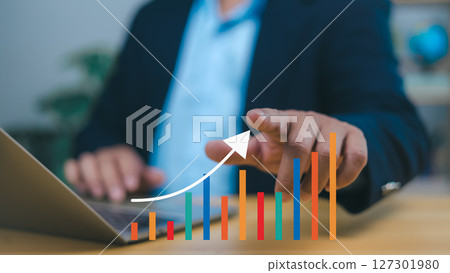 Person hand points to an upward-trending bar graph with a white arrow, symbolizing positive business growth, financial success, increasing market trends. Conveys prosperity and strategic progress. Person hand points to an upward-trending bar graph with a white arrow, symbolizing positive business growth, financial success, increasing market trends. Conveys prosperity and strategic progress. 127301980