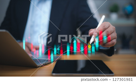 A businessman uses a stylus to analyze a dynamic, fluctuating financial graph with red and blue bars, symbolizing investment analysis, stock market trends, and data driven decision making. A businessman uses a stylus to analyze a dynamic, fluctuating financial graph with red and blue bars, symbolizing investment analysis, stock market trends, and data driven decision making. 127301981
