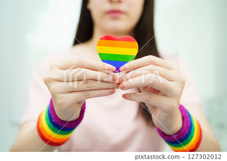 Asian woman holding LGBT heart with rainbow flag. Asian woman holding LGBT heart with rainbow flag. 127302012