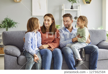 Happy family gathered on sofa listening attentively to their cheerful son sharing his news of day. 127302584