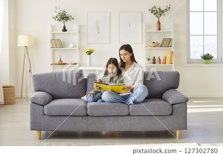 Mother and daughter reading book, story on sofa, happy time at home, joy with preschool child  127302780