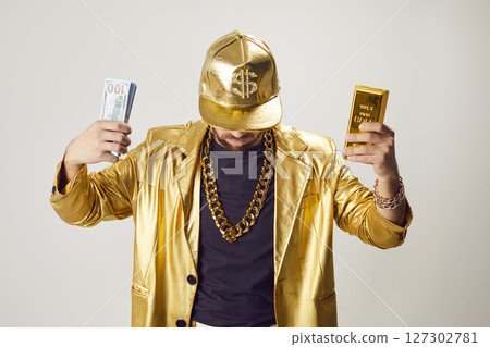 Funny man in golden suit holding money cash and gold bar on white studio background. 127302781