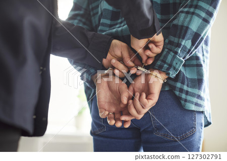 Police officer is arresting a male criminal and putting hand cuffs on his wrists 127302791