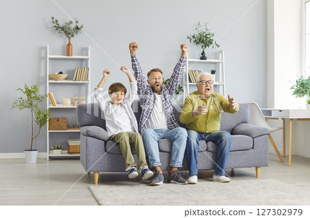 Excited grandfather, father and child boy sitting on sofa at home watching football game on TV 127302979