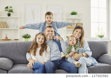 Portrait of young happy family with kids sitting on sofa at home and looking at camera together. Portrait of young happy family with kids sitting on sofa at home and looking at camera together. 127302982
