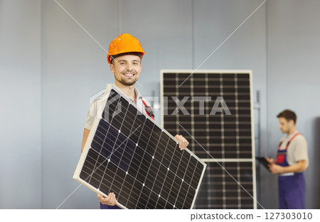 Man in protective helmet holding photovoltaic panel and smiling. 127303010