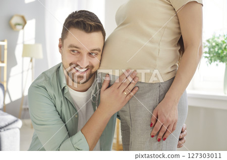Happy man listening to his beautiful pregnant woman's tummy and smiling sanding at home. Happy man listening to his beautiful pregnant woman's tummy and smiling sanding at home. 127303011