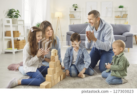 Happy parents playing educational game with children, building wooden block tower together at home. 127303023