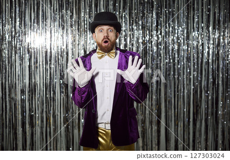 Funny extravagant man, magician, conjurer in shining glittering jacket, hat, feels excited  127303024