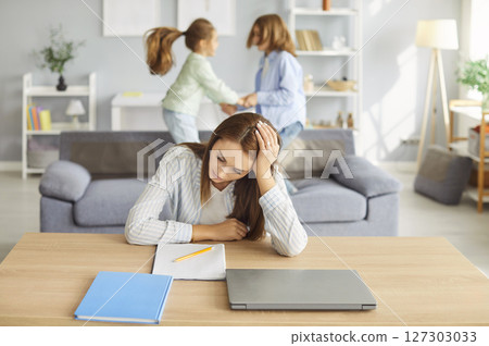 Young tired woman in noisy room, nanny, baby sitter mother suffers from headache touching head Young tired woman in noisy room, nanny, baby sitter mother suffers from headache touching head 127303033