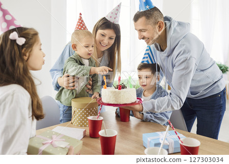 Toddler boy is having delightful birthday celebration surrounded by family members. 127303034