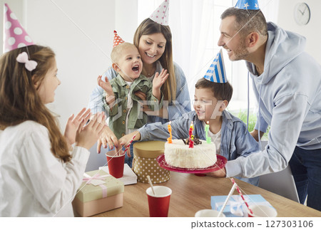 Happy joyful family in festive cap celebrating birthday together in living room at home. 127303106