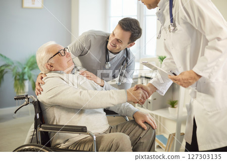 Doctor And Nurse Shaking Hands With Patient In Wheelchair During Consultation Doctor And Nurse Shaking Hands With Patient In Wheelchair During Consultation 127303135
