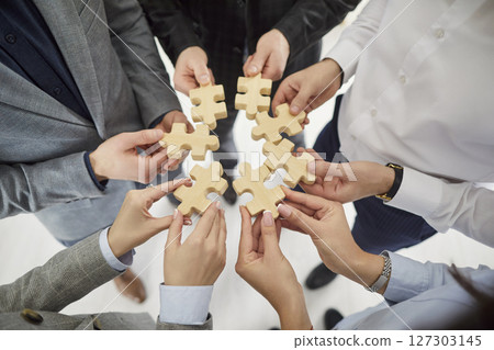 Hands of a group of business people assembling wooden puzzle in office. Team work. 127303145