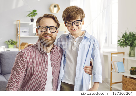 Portrait of a happy young father hugging his cute little child boy wearing eyeglasses at home. 127303204