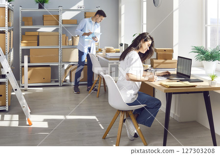 Woman working in logistics center with male colleague preparing order for client in warehouse 127303208