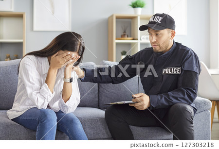 Police officer talking to female robbery victim after burglary sitting on sofa at home. Police officer talking to female robbery victim after burglary sitting on sofa at home. 127303218