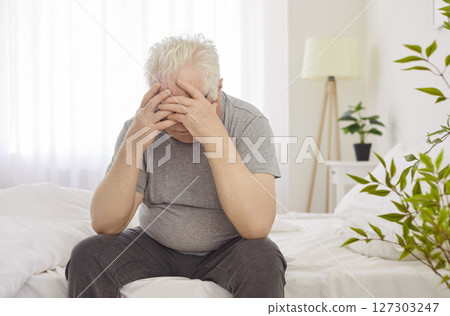 Senior elderly stressed man suffering from headache sitting on bed in bedroom at home. Senior elderly stressed man suffering from headache sitting on bed in bedroom at home. 127303247