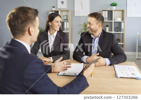Business man financial advisor consulting young couple sitting on workplace in office. 127303266