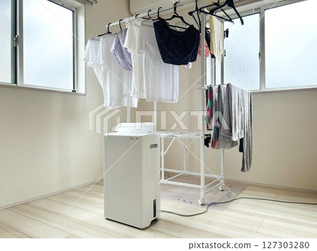A clothes drying stand installed in a room and a dehumidifier in operation. Drying clothes indoors during the rainy season A clothes drying stand installed in a room and a dehumidifier in operation. Drying clothes indoors during the rainy season 127303280