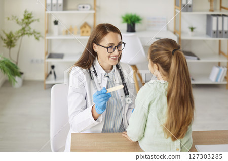 Smiling woman doctor with spatula asks child to open mouth for throat examination 127303285