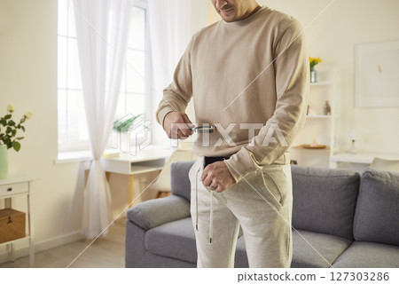 Concerned young man using magnifying glass to examine lower body while checking health condition. 127303286