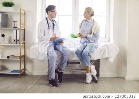 Portrait of a male doctor talking with young female patient sitting on couch in clinic in exam room 127303312