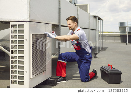 Technician installing and fixing air conditioner using screwdriver sitting on the roof of building. 127303315