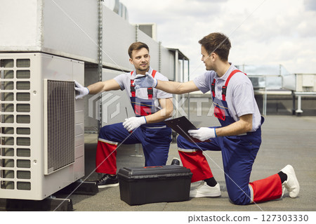 Team of young professional technicians sitting on rooftop and installing air conditioner. 127303330