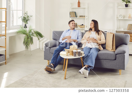 Couple resting after a lunch delivered by delivery service sitting on sofa at home. Couple resting after a lunch delivered by delivery service sitting on sofa at home. 127303358