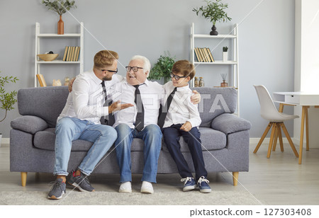 Happy grandfather, father and little child boy wearing eyeglasses sitting at home and talking 127303408