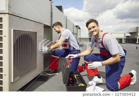 Smiling Electrician Installing HVAC System on Roof 127303412