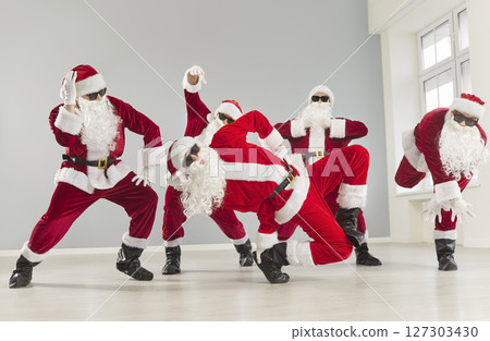 Happy funny men in Santa Claus costumes and sunglasses celebrating New Year dancing in empty room. Happy funny men in Santa Claus costumes and sunglasses celebrating New Year dancing in empty room. 127303430