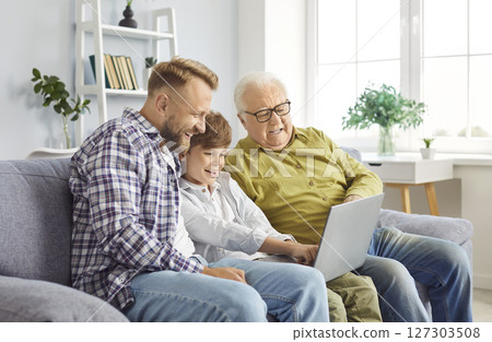Happy little child boy with father and grandfather sitting on sofa using laptop together 127303508